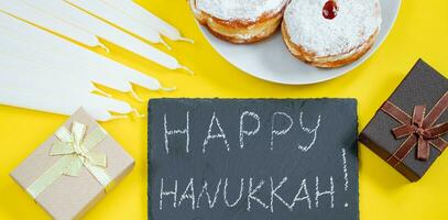 Feliz Hanukkah. sobremesa judaica sufganiyot em fundo amarelo. símbolos do feriado religioso do judaísmo. rosquinhas, velas e presente. foto