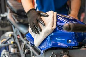 motociclista limpando motocicleta, cera polida e de revestimento no tanque de combustível na garagem. conceito de manutenção e reparo de motocicleta. foto