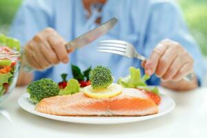 ásia idosos mulher paciente comendo salmão estaca e vegetal salada para saudável Comida dentro hospital. foto