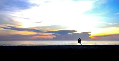 silhueta do uma casal caminhando em a de praia dentro a manhã foto