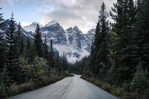 dirigindo na estrada em uma floresta de pinheiros com montanhas rochosas no lago Moraine foto