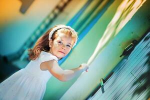 a pequeno menina dentro uma azul vestir bate em a janela. a criança retornou lar. a menina estava indo para escola em pé em a varanda perto a escadas em a fundo do de madeira portas foto