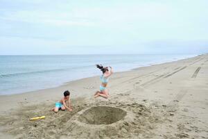 crianças escavação uma orifício dentro a areia em a Beira Mar. foto
