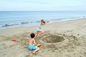 crianças escavação uma orifício dentro a areia em a Beira Mar. foto