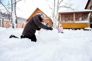 uma família constrói uma boneco de neve Fora do branco neve dentro a Jardim dentro inverno. foto