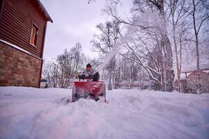 uma jovem homem limpa neve com uma neve ventilador dentro dele quintal. foto