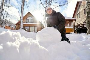 uma família constrói uma boneco de neve Fora do neve dentro a Jardim dentro inverno. foto