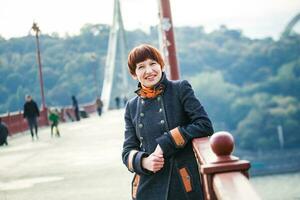 jovem mulher em pé em uma pedestre ponte dentro Kiev. a mulher com curto cabelo inclinado em a ponte corrimão. mulher em a fundo do Kiev panorama. foto