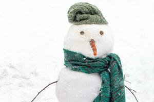 boneco de neve em fundo do neve deriva durante queda de neve dentro inverno. neve figura com verde tricotado cachecol e chapéu. foto