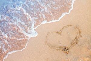 uma onda este lavagens a coração pintado em a areia. uma memória do uma feliz feriado de a oceano. foto