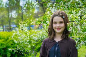 lindo menina entre cereja flores dentro Primavera. retrato do uma menina com Castanho cabelo e verde olhos. foto