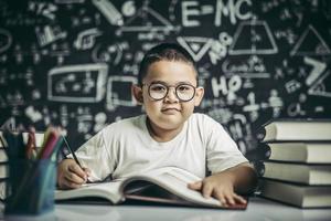 um menino de óculos escrevendo na sala de aula foto