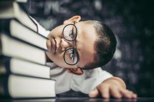 um menino de óculos sentado na sala de aula contando livros foto