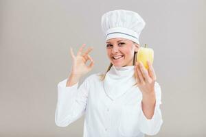lindo fêmea chefe de cozinha é mostrando Pimenta e Está bem placa em cinzento fundo. foto