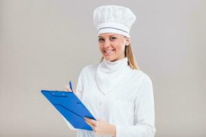 lindo fêmea chefe de cozinha é segurando livro de receitas e escrevendo uma Novo receita. foto