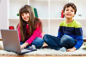 dois crianças sentado em a chão com uma computador portátil foto