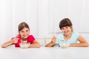 fofa pequeno meninas estão sentado e comendo cereais para café da manhã foto