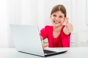 fofa pequeno menina é usando laptop.e mostrando polegar acima. foto