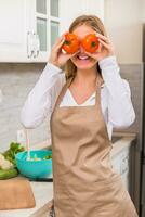 lindo mulher cobertura olhos com tomate enquanto fazer refeição dentro dela cozinha foto