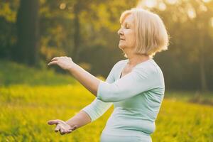 Senior mulher goza exercício tai chi dentro a natureza foto