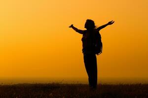 silhueta do uma mulher caminhante cumprimento a pôr do sol foto