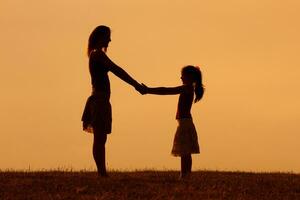 silhueta do mãe e filha segurando mãos dentro a natureza foto