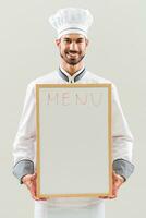 chefe de cozinha é segurando quadro branco em cinzento fundo. foto