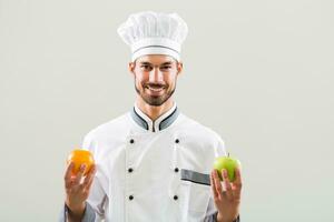 chefe de cozinha é segurando maçã e laranja em cinzento fundo foto