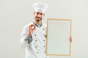 chefe de cozinha é mostrando quadro branco e Está bem placa em cinzento fundo. foto