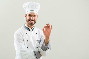 sorridente chefe de cozinha mostrando Está bem placa em cinzento fundo foto