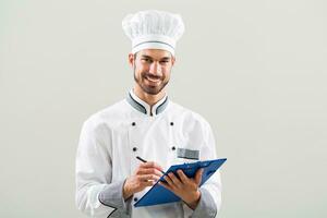 sorridente chefe de cozinha é segurando livro de receitas e escrevendo uma Novo receita. foto