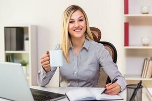 empresária bebendo café enquanto trabalhando dentro dela escritório foto