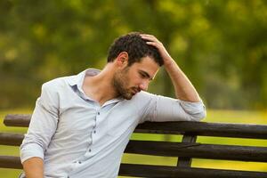 depressivo homem de negocios é sentado às a parque e pensando sobre alguma coisa foto