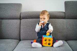 fofa pequeno bebê Garoto jogando com brinquedos enquanto sentado em sofá foto