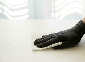 mão dentro uma Preto nitrilo luva lenços a mesa com desinfetante solução. seletivo foco foto