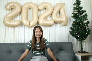 ásia mulher vestido Como uma favela feliz esperando para comemoro Natal 2024. decorar e decorar a quarto com Natal árvore e 2024 balões. foto