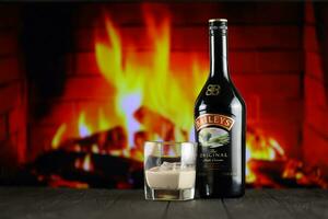 kyiv, ucrânia - 4 de maio de 2022 garrafa de álcool original de baileys na mesa de madeira com lareira vermelha foto