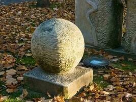 uma escultura dentro a Formato do uma bola em uma quadrado pedestal dentro uma cidade parque. a jogar do luz em a superfície do a bola. foto