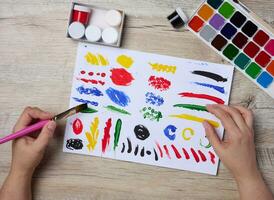 conjunto do aguarela tintas, escovas e papel com diferente golpes e cores. fêmea mãos segurando uma escova foto