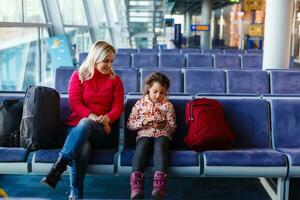 adorável criança pequena menina e dela mãe esperando às a aeroporto com bagagem, viajando com crianças, família férias, Tempo às a esperando quarto foto