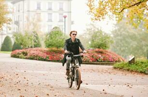 ao ar livre retrato do bonito cabelo lido homem equitação bicicleta dentro uma cidade foto