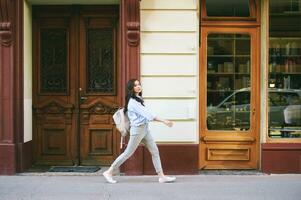 ao ar livre retrato do lindo jovem mulher caminhando baixa a rua, vestindo mochila foto