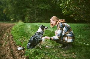 ao ar livre retrato do lindo jovem mulher jogando com australiano pastor cachorro, segurando uma pata foto