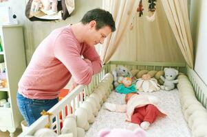 pai admirando quão recém-nascido bebê dormindo dentro berço, primeiro dias do vida foto
