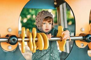 ao ar livre retrato do feliz sorridente criança pequena menina tendo Diversão em Parque infantil, frio clima foto