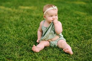 ao ar livre retrato do adorável 6 meses velho bebê menina jogando dentro verão parque, criança rastejando em fresco verde gramado foto