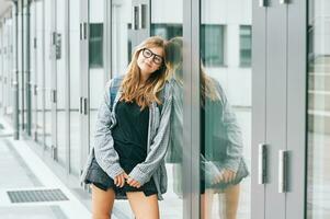 ao ar livre retrato do jovem Adolescência criança menina vestindo óculos e mochila, inclinado em a parede foto