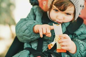 feliz criança pequena criança comendo fruta bar, saudável lanche, sentado dentro carrinho de criança foto