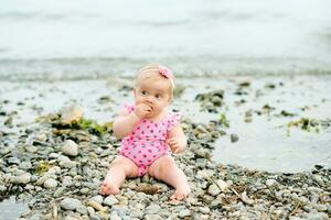 ao ar livre retrato do adorável bebê menina jogando com algas marinhas de a rio, vestindo Rosa roupa de banho foto