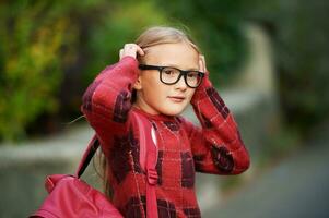 ao ar livre retrato do adorável pequeno menina caminhando para escola, sendo mochila e óculos foto